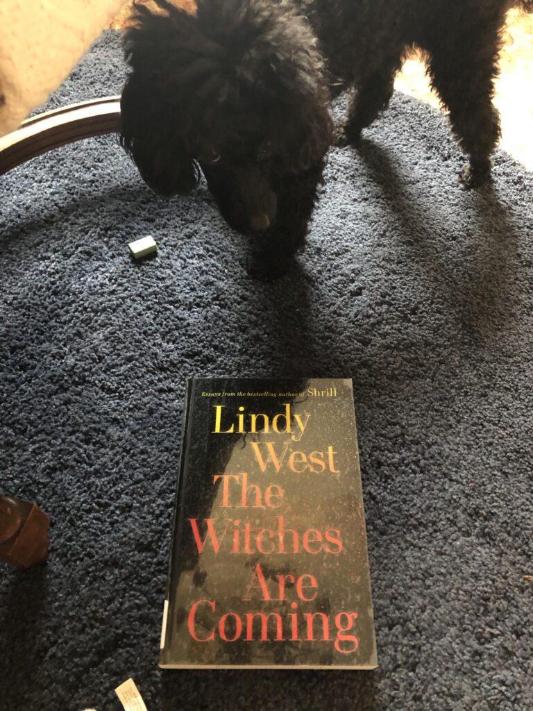 My dog Rosie on a blue carpet with the book "The Witches Are Coming" by Lindy West